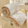 A rolled up white floral quilt with pink lining resting on a lace tablecloth.