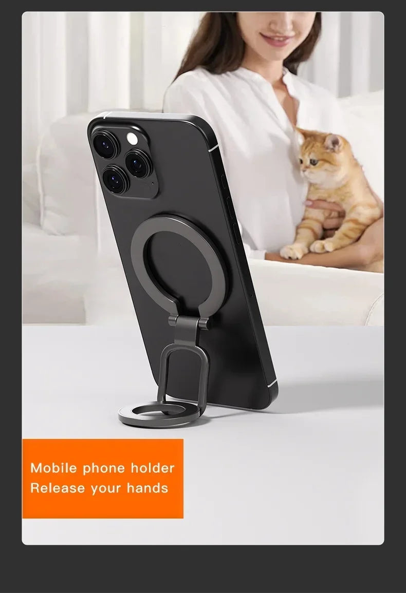 Black magnetic phone holder with a ring and kickstand resting on a white table.