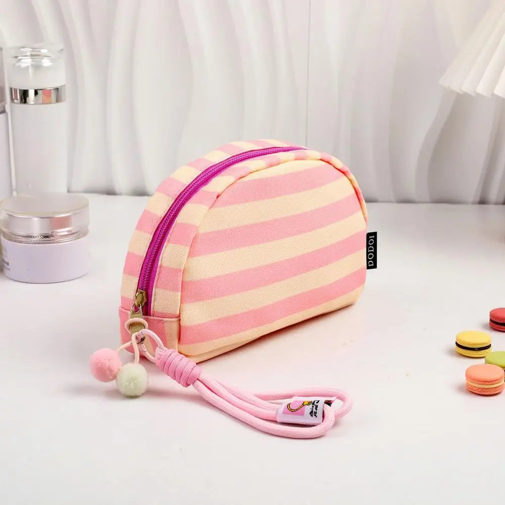 Pochette en crochet rayée rose et blanc avec fermeture éclair violette et cordon rose, exposée sur une surface blanche.