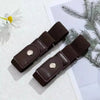 A pair of dark brown elastic belts are displayed on a white surface next to a green branch and white flower.