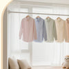 A collection of light-colored shirts hanging on a shower curtain rod in a bright window setting.