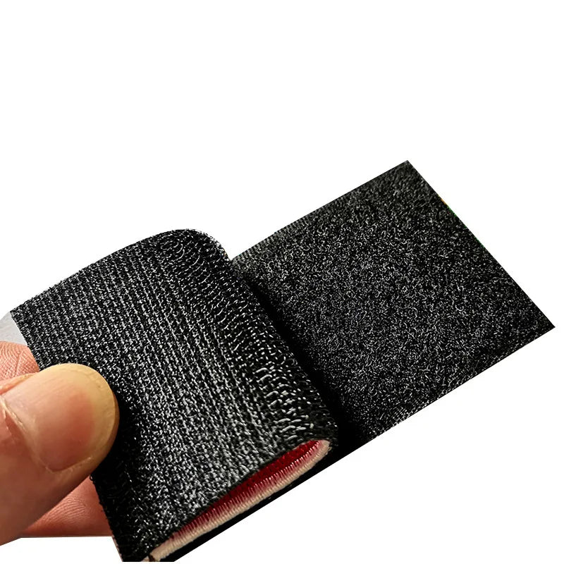 A hand holds an embroidered hook and loop patch with reflective accents, showing the texture and detail of the fabric.