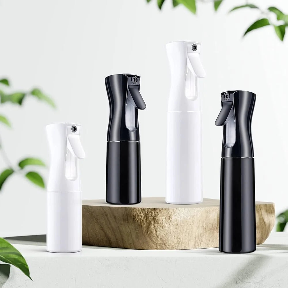 A set of black and white continuous fine mist spray bottles for hair, plants, and home use displayed on a wooden surface.