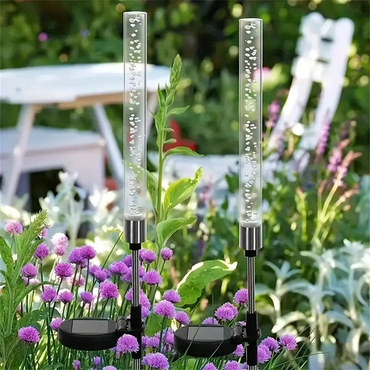 A vertical glass light fixture with a solar panel base is shown in a garden setting.