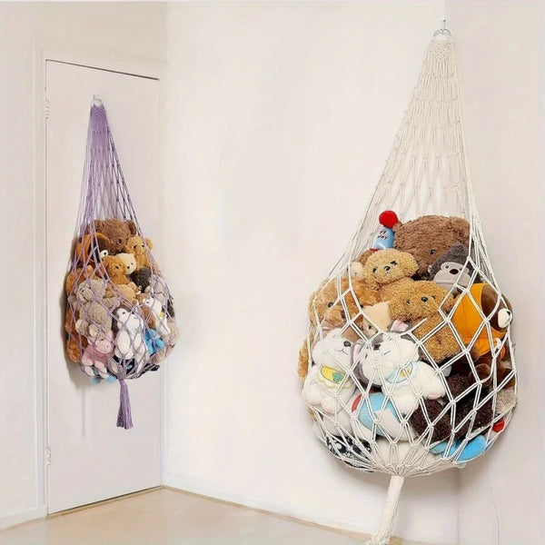 Macramé-Hängematte gefüllt mit verschiedenen Plüschtieren an einer weißen Wand.