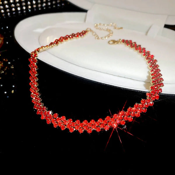 A close-up of a red geometric rhinestone choker necklace displayed on a white plate.