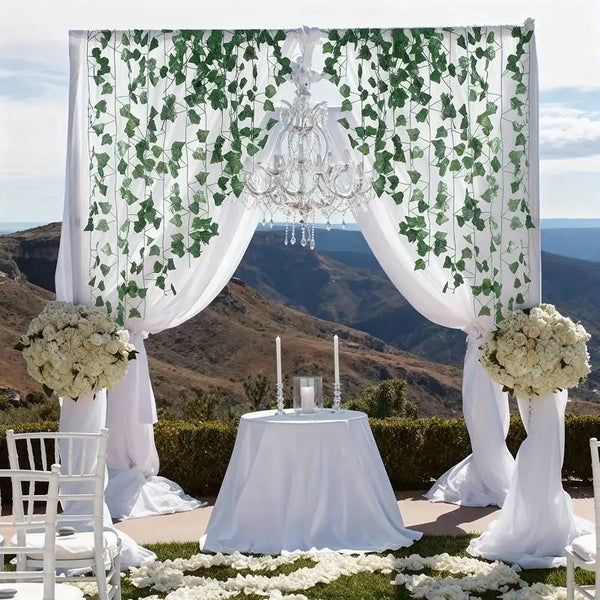 A wedding arch decorated with white draping and green ivy garlands framing a table.