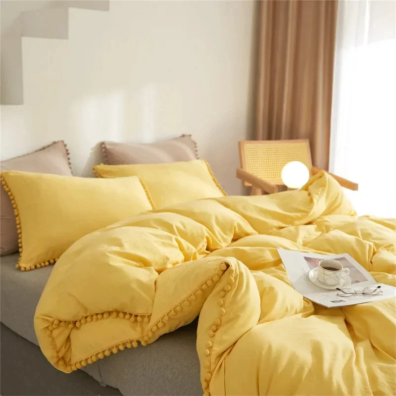 Yellow duvet cover set with pom tassels on a bed in a bright room.
