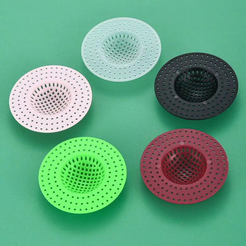 Five colored silicone sink drain filters or strainers arranged on a green surface.