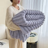 A person is holding a large, fluffy, lavender fleece blanket with white trim against a bright window background.