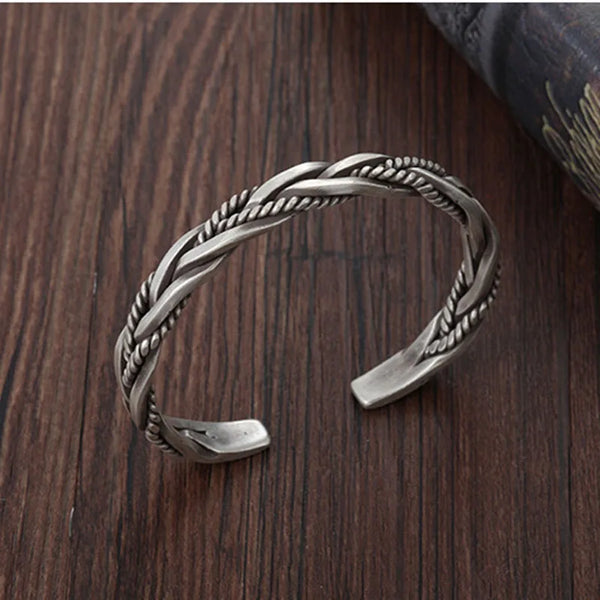 Bracelet à manche torsadé en argent sterling sur une surface en bois foncé.
