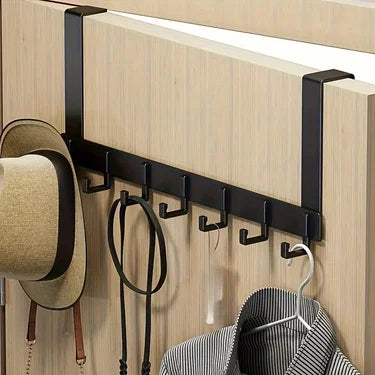 A black over-the-door coat rack with six hooks mounted on a light wood cabinet door.