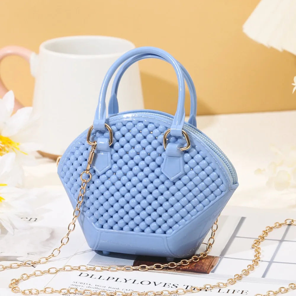 Sac bandoulière en gelée bleu clair avec bracelet doré posé sur une surface en bois.