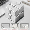 Silver metal infinity fidget cube with rounded corners shown on a white desk.