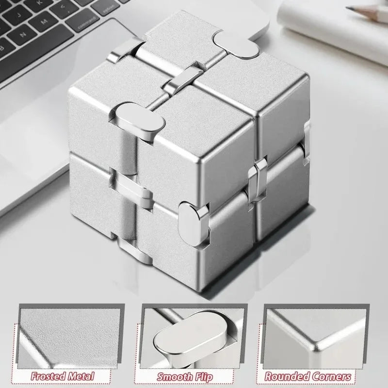 Silver metal infinity fidget cube with rounded corners shown on a white desk.