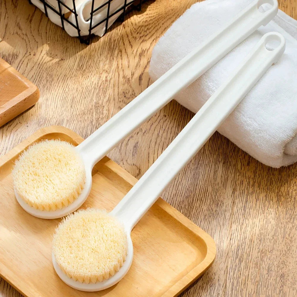 Cepillo ergonómico blanco de mango largo con cerdas amarillas sobre una bandeja de madera junto a una toalla blanca.