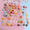 A collection of miniature resin food and drink figurines in various colors and shapes arranged on pink paper.