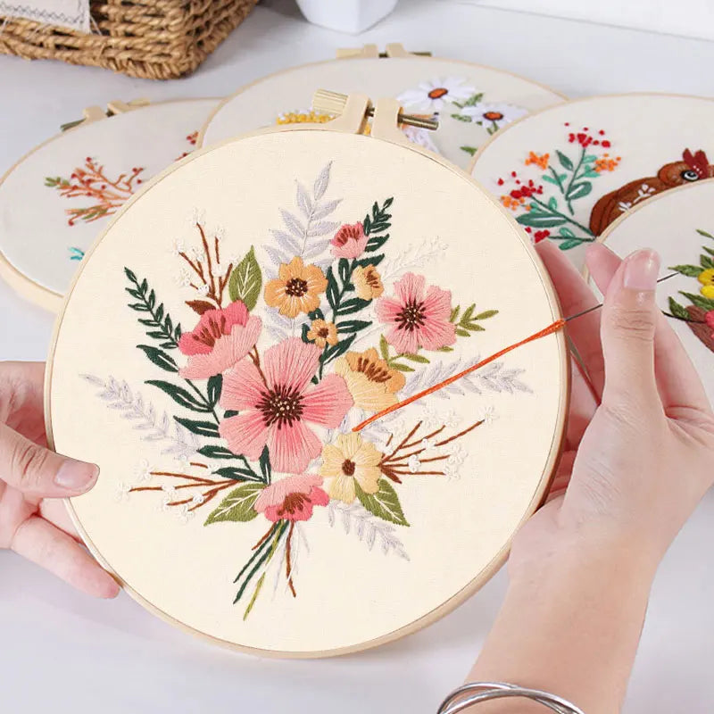 Hands are embroidering a floral design on a round canvas with a needle and thread.