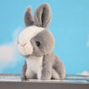 A gray and white mini plush bunny toy with large ears and a pink nose sitting on a surface against a light blue background.