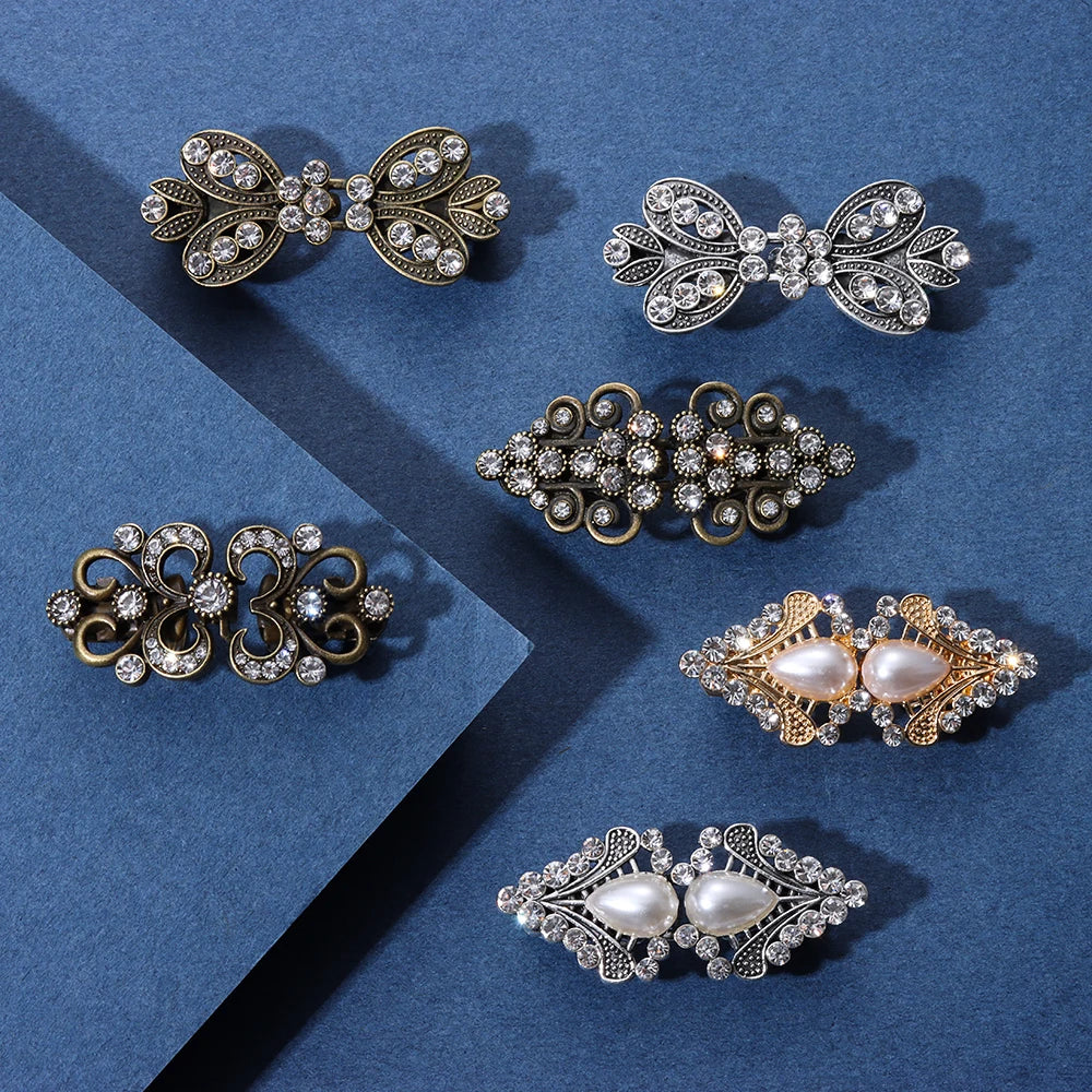 A collection of vintage-style floral and swirl metal clips made with clear and white stones for clothing.