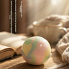 A smooth, multicolored stress ball rests on a wooden surface next to a book and soft fabric.