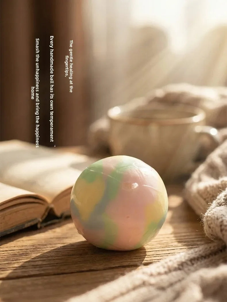 A smooth, multicolored stress ball rests on a wooden surface next to a book and soft fabric.