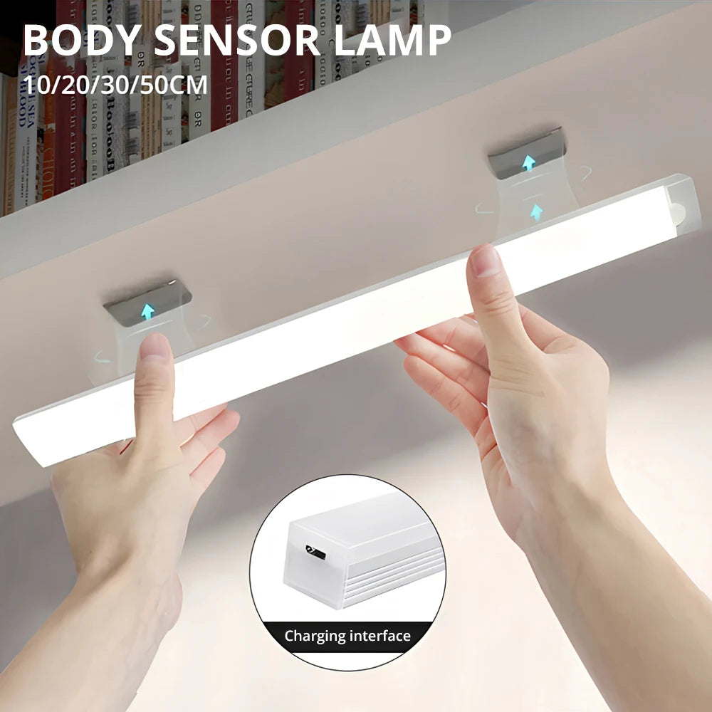 Hands hold a white body sensor lamp with magnetic mounts, showing the light emitting from the strip.
