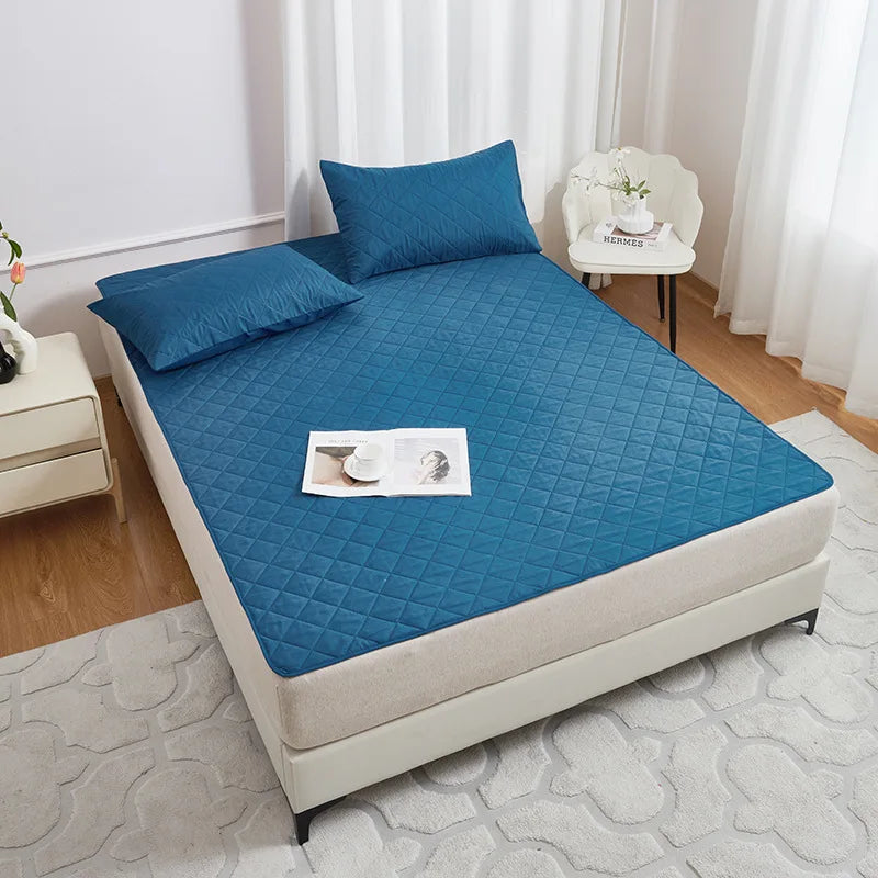 A teal waterproof mattress protector with elastic straps is displayed on a bed, next to a white chair and a bedside table.