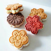 A set of three floral cookie cutters in peach, cherry blossom, and sunflower designs resting on a white surface.