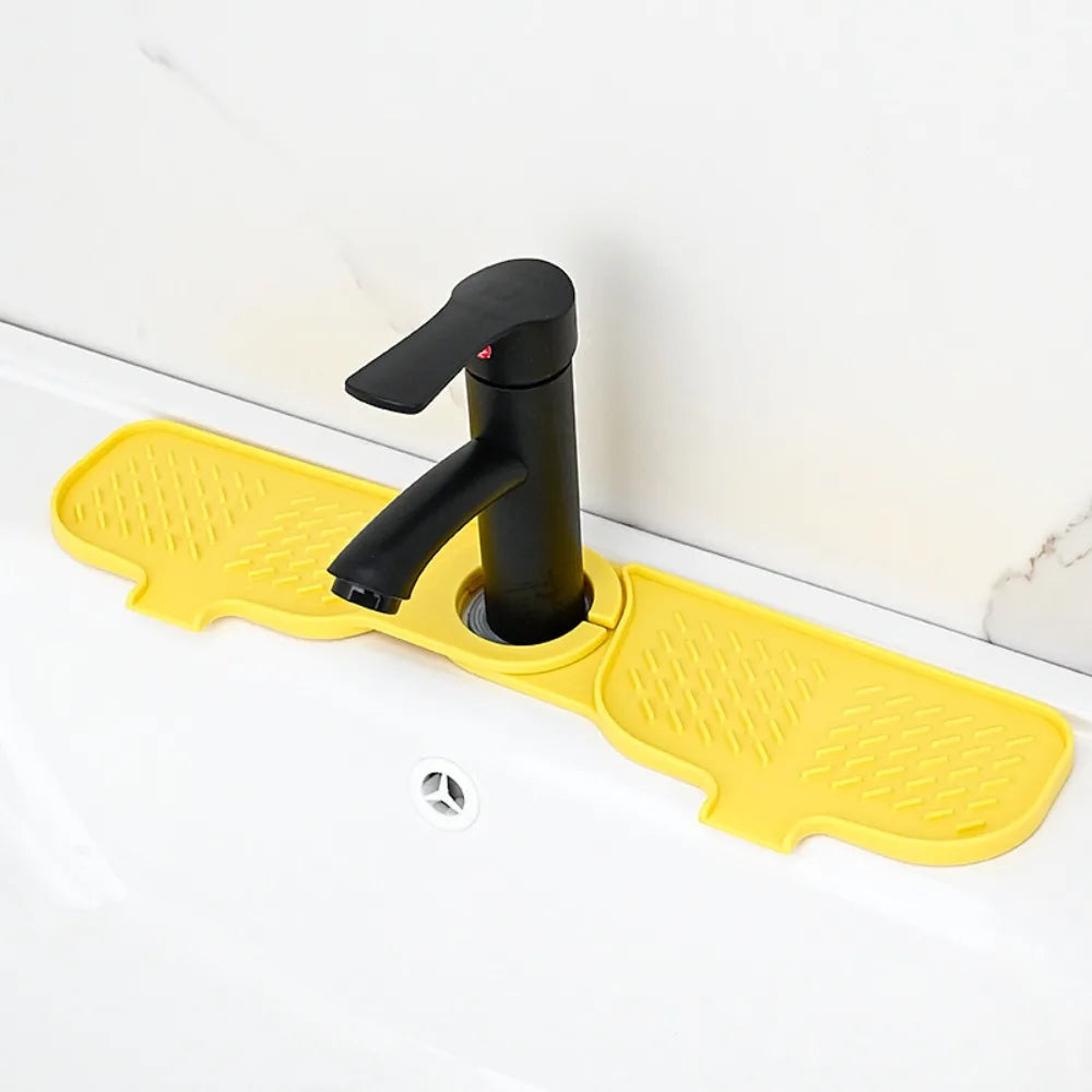 A black silicone faucet mat with a yellow, textured splash guard is installed on a white kitchen sink.