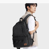 A man wearing a beige jacket and white shirt is carrying a black Lee ultralight water-resistant laptop backpack.