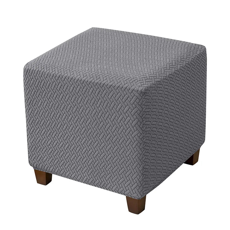 A gray stretch jacquard ottoman slipcover with an elastic edge.