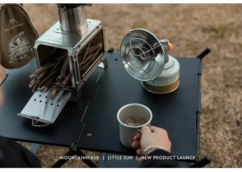A portable butane gas stove is set up on a dark surface outdoors, with wood fuel and a metal strainer visible.