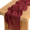 A deep maroon cotton gauze table runner draped over a light wood surface.