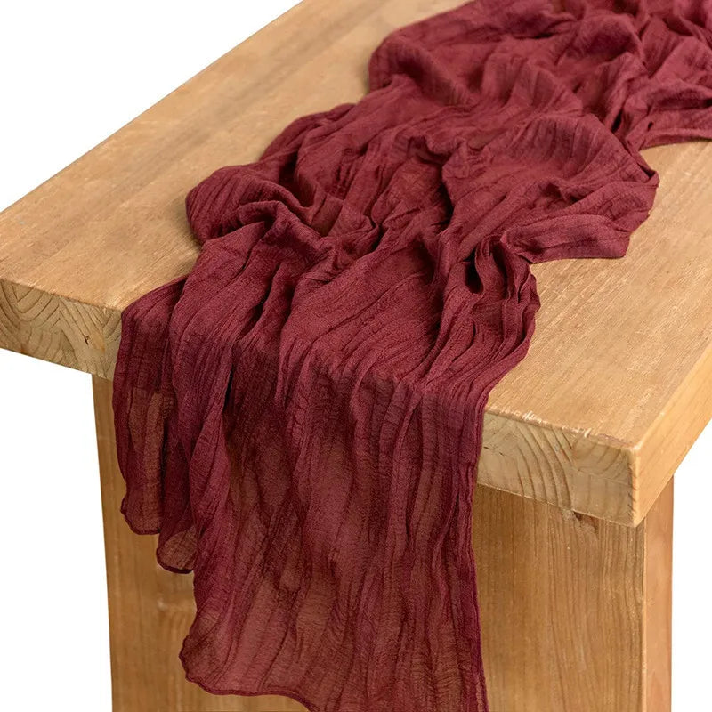 A deep maroon cotton gauze table runner draped over a light wood surface.