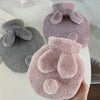 A hand holds a soft, fluffy pink plush rabbit hot water bottle with a matching flannel cover.