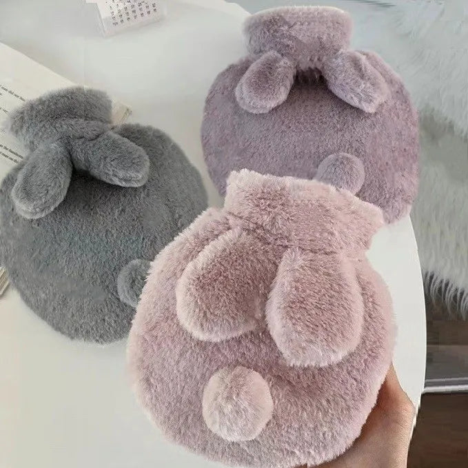 A hand holds a soft, fluffy pink plush rabbit hot water bottle with a matching flannel cover.