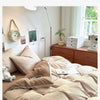 A bed with a beige duvet cover set and pillows, next to a wooden dresser and a plant.