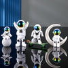 A set of handcrafted astronaut figurines in white resin and glass eyes displayed on a reflective surface.