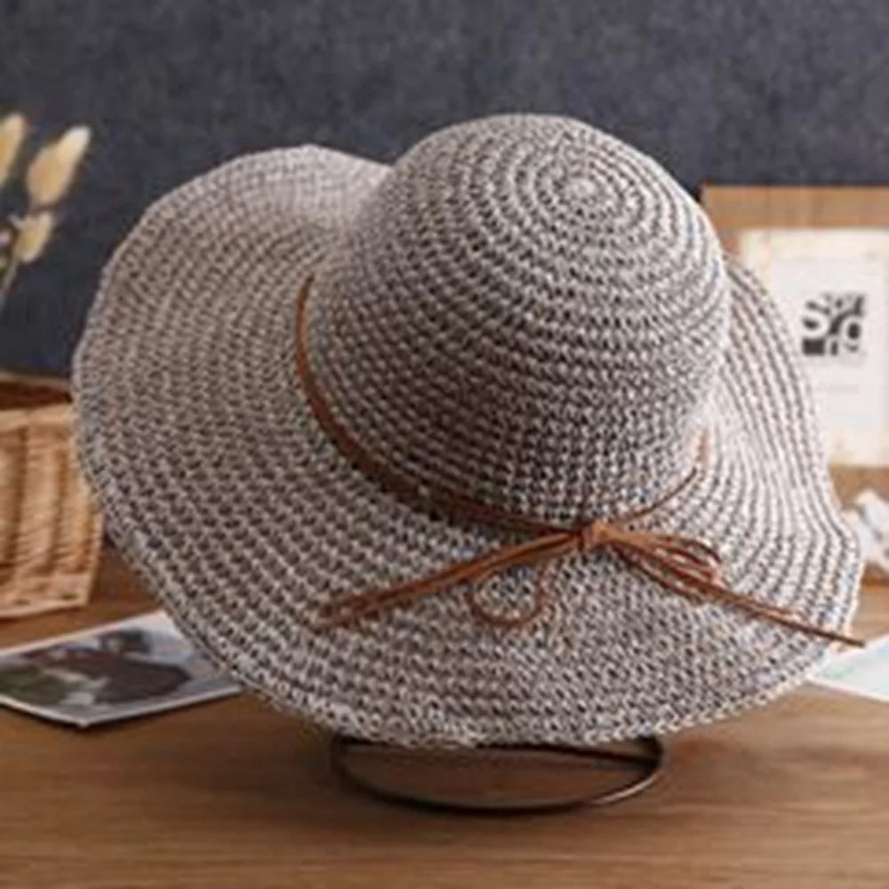 Sombrero de paja de ala ancha con textura tejida y cinta de cuero marrón sobre una superficie de madera.
