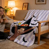 A woman sits on a sofa holding a mug while a striped blanket with a witch design is draped over the couch.