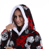 Eine lächelnde Frau trägt einen oversized Fleece-Hoodie mit schwarzem und rotem Patchwork-Totenkopfmuster und weißer Sherpa-F