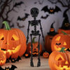 A black skeletal figure stands in front of glowing orange jack-o'-lanterns on a wooden surface.
