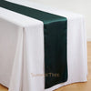Elegant satin table runner in dark green placed on a white tablecloth.