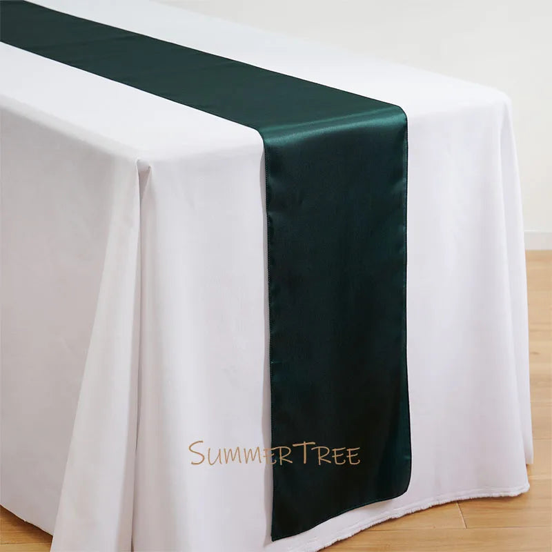 Elegant satin table runner in dark green placed on a white tablecloth.