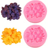 A set of three pink silicone molds shaped like flowers in purple, orange, and pink colors.