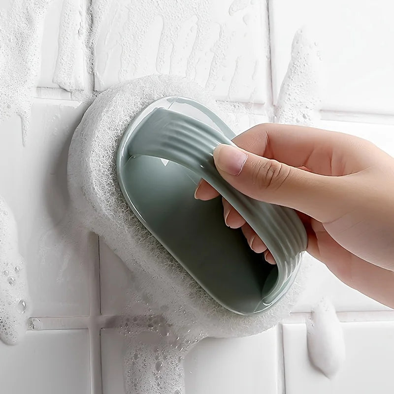 A hand is holding a green magic sponge scrubber with a long handle against a white tiled surface.