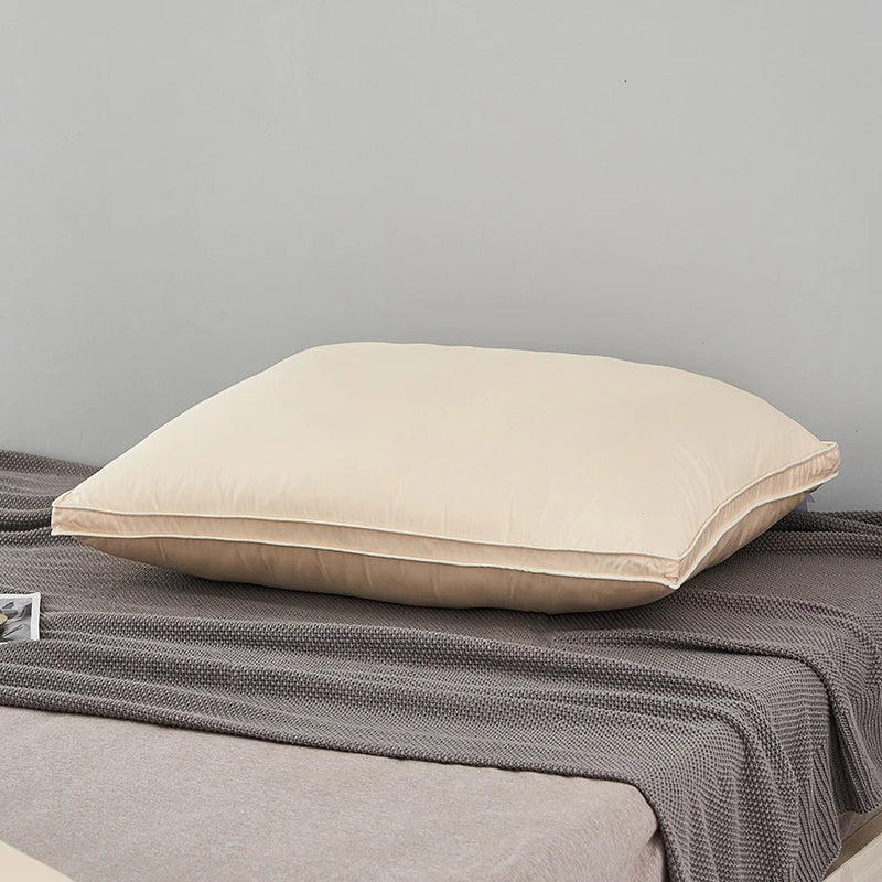 A cream-colored luxury goose down and feather pillow with a light beige cotton cover resting on a gray fabric.