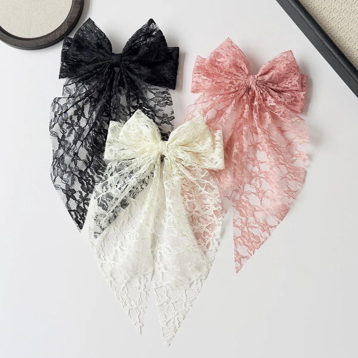 Three lace bows in black, pink, and cream are displayed on a white surface.