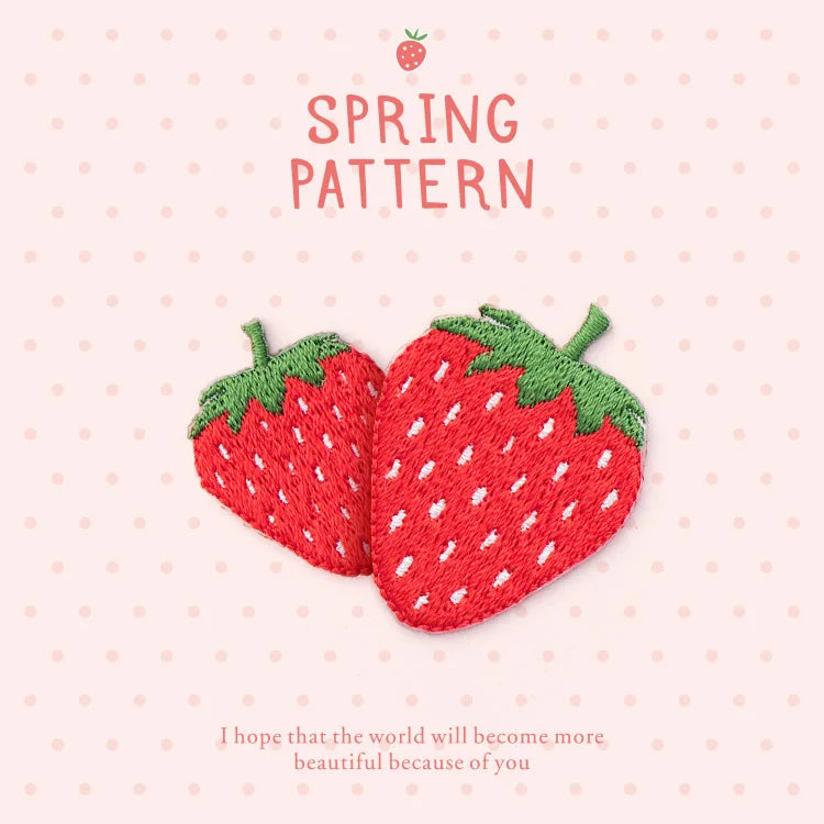 A red strawberry embroidery patch with green leaves and seeds on a light pink background.